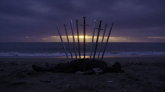 Карта Таро Десятка Мечей: фигура на берегу моря с десятью мечами в спине на фоне начинающегося рассвета.