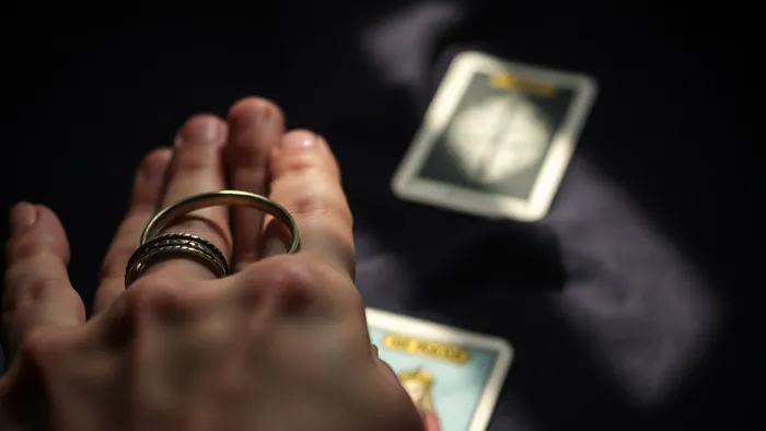 Крупный план женских рук, держащих винтажное кольцо. На размытом фоне на бархатной ткани лежит карта Таро Жрица. Драматическое освещение создает таинственную атмосферу.