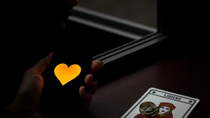 Символичное изображение дилеммы виртуальной измены: телефон с сердечком, карта Таро 'Влюбленные' и обручальное кольцо в полумраке.