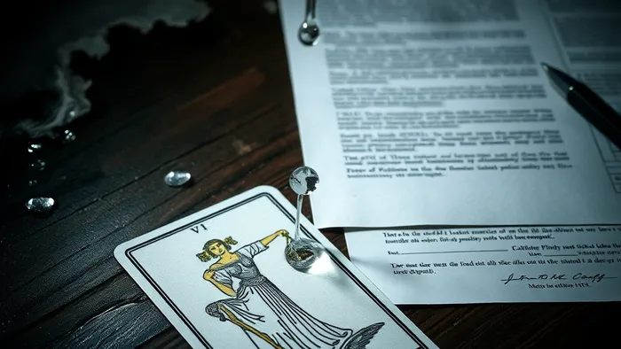 Аркан Правосудие из колоды Таро лежит рядом с фрагментом поврежденного водой потолка и юридическими бумагами на столе.